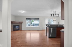 Hardwood-finish flooring, built-in fireplace with stone surround and wood mantel, stainless steel dishwasher, and contemporary chandelier - 