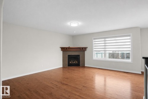 Hardwood flooring, fireplace with wood mantel, large window with blinds, and flush-mount ceiling light - 8432 18 Avenue Sw, Edmonton, AB - Indoor Photo Showing Living Room With Fireplace