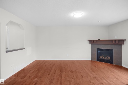 Wood-finish flooring, corner fireplace with tile surround, wood mantel, recessed lighting, and pass-through window with sill - 8432 18 Avenue Sw, Edmonton, AB - Indoor With Fireplace