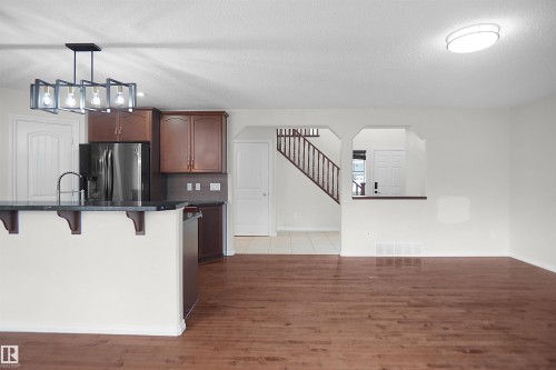 Open concept living area with wood-finish flooring, a kitchen island with stone countertop, stainless steel appliances, and a contemporary chandelier - 8432 18 Avenue Sw, Edmonton, AB - Indoor Photo Showing Kitchen With Upgraded Kitchen