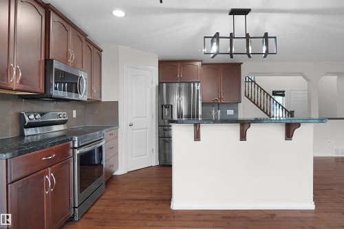 Kitchen featuring wood-finish flooring, dark cabinetry, stainless steel appliances, and a breakfast bar with dark countertops - 8432 18 Avenue Sw, Edmonton, AB - Indoor Photo Showing Kitchen