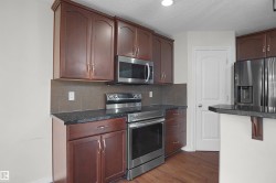Kitchen featuring dark wood cabinetry, stainless steel appliances, dark stone countertops, and a tile backsplash - 