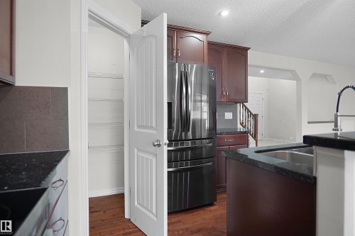 Cherry-finish cabinetry with dark countertops, stainless steel appliances, and a double basin sink with a high-arc faucet - 8432 18 Avenue Sw, Edmonton, AB - Indoor Photo Showing Kitchen