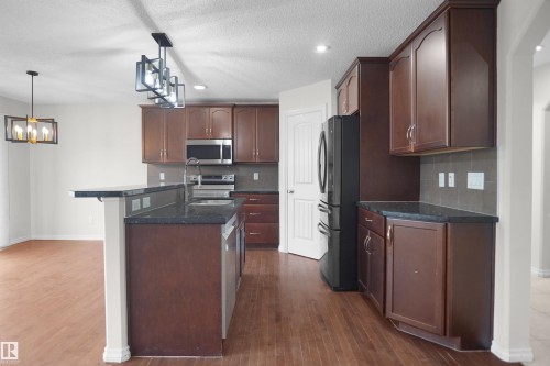 Kitchen featuring wood-finish flooring, dark wood cabinetry, dark countertops, a stainless steel sink, and stainless steel appliances - 8432 18 Avenue Sw, Edmonton, AB - Indoor Photo Showing Kitchen