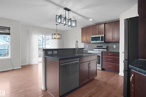 Kitchen featuring a central island with an integrated sink, dark cabinetry, and stainless steel appliances - 8432 18 Avenue Sw, Edmonton, AB - Indoor Photo Showing Kitchen