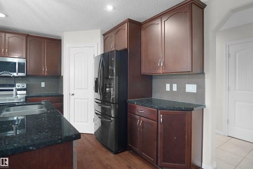 Dark wood-finish cabinetry with silver-tone hardware, dark countertop surfaces, stainless steel appliances, and wood-finish flooring - 8432 18 Avenue Sw, Edmonton, AB - Indoor Photo Showing Kitchen With Double Sink