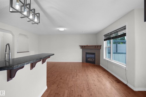 Wood-finish flooring, built-in fireplace, granite-look countertop, pendant light fixtures, and a large window with blinds - 8432 18 Avenue Sw, Edmonton, AB - Indoor With Fireplace