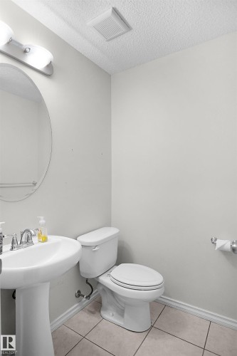Pedestal sink with chrome faucet, oval wall mirror, and tile flooring - 8432 18 Avenue Sw, Edmonton, AB - Indoor Photo Showing Bathroom