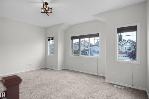 Spacious room featuring carpeting, multiple windows with blinds, a contemporary ceiling light fixture, and freshly painted walls - 8432 18 Avenue Sw, Edmonton, AB - Indoor Photo Showing Other Room