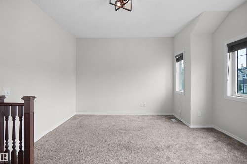 Carpeted room with light neutral wall paint, two windows with roller shades, and a decorative ceiling light fixture - 8432 18 Avenue Sw, Edmonton, AB - Indoor Photo Showing Other Room