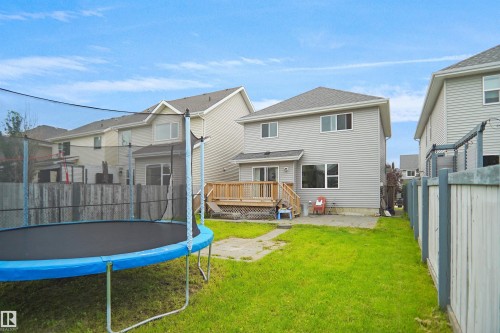 Rear exterior featuring light grey siding, a wood deck with stairs, and a modest lawn area - 8432 18 Avenue Sw, Edmonton, AB - Outdoor