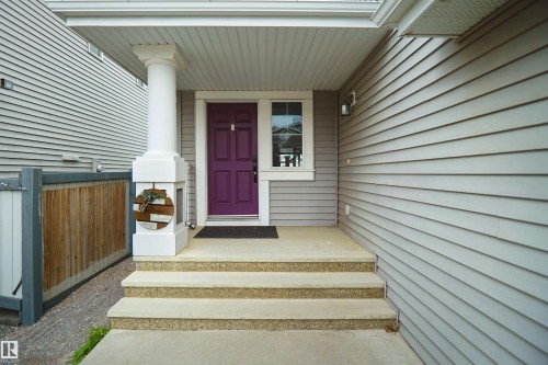 Welcoming front entry featuring a bold plum-painted door, white column support, sidelite window, and composite stepped landing - 8432 18 Avenue Sw, Edmonton, AB - Outdoor With Exterior