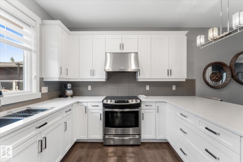 Modern kitchen featuring white shaker-style cabinetry with stainless steel hardware, quartz countertops, stainless steel range hood, and a black slide-in range with convection oven - 5616 Juchli Avenue Nw, Edmonton, AB - Indoor Photo Showing Kitchen