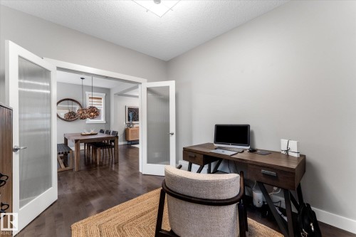 Home office featuring a wood-finish desk with ample work surface, a comfortable upholstered chair, and a wall-mounted flat-screen television - 5616 Juchli Avenue Nw, Edmonton, AB - Indoor Photo Showing Office