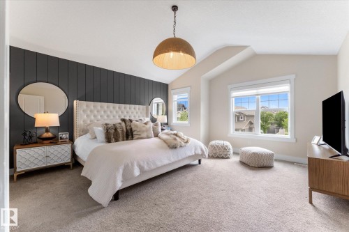 Spacious primary bedroom featuring a tufted upholstered headboard, pendant lighting, and abundant natural light from oversized windows - 5616 Juchli Avenue Nw, Edmonton, AB - Indoor Photo Showing Bedroom