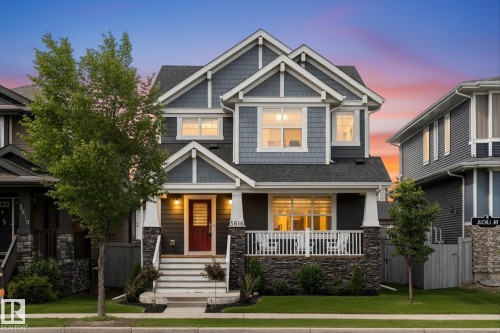 Two-story exterior with a covered front porch featuring white railings, stone accents, and a contrasting red entry door - 5616 Juchli Avenue Nw, Edmonton, AB - Outdoor With Deck Patio Veranda With Facade