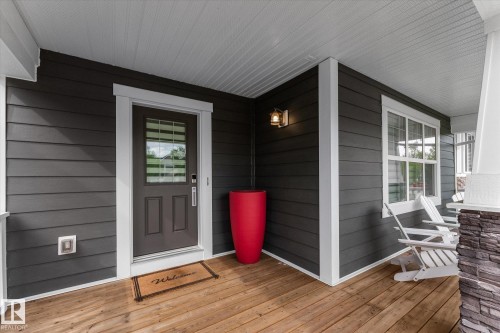 Welcoming front entry featuring a dark horizontal-plank exterior with white trim, six-panel entry door with transom window, and warm wood-finish flooring - 5616 Juchli Avenue Nw, Edmonton, AB - Outdoor With Deck Patio Veranda With Exterior