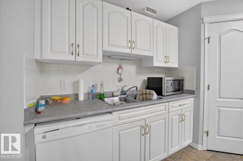 White cabinetry with decorative fronts, integrated dishwasher, light gray countertops, and a tile backsplash - #116 237 Youville Dr E Nw, Edmonton, AB - Indoor Photo Showing Kitchen With Double Sink