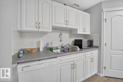White cabinetry with decorative fronts, integrated dishwasher, light gray countertops, and a tile backsplash - 
