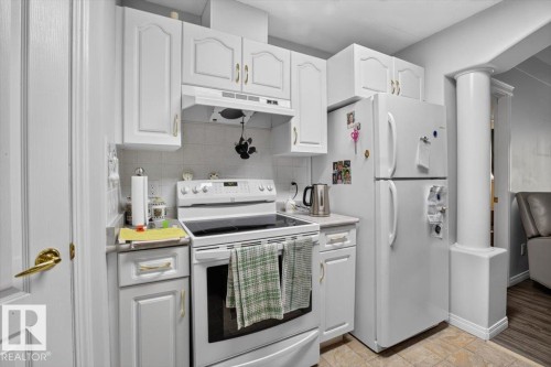 White cabinetry with gold-tone hardware, white range, white refrigerator, and tiled flooring - #116 237 Youville Dr E Nw, Edmonton, AB - Indoor Photo Showing Kitchen