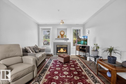 Living area featuring wood-finish flooring, a built-in fireplace with a stone surround, and light-toned walls - #116 237 Youville Dr E Nw, Edmonton, AB - Indoor Photo Showing Living Room With Fireplace