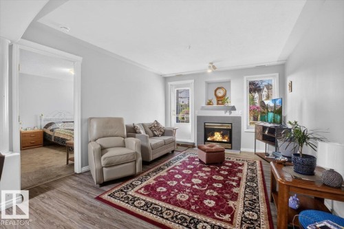 Living area featuring wood-finish flooring, a built-in fireplace with a stone surround, and an adjacent window - #116 237 Youville Dr E Nw, Edmonton, AB - Indoor Photo Showing Living Room With Fireplace