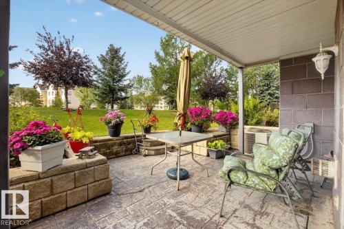 Covered patio featuring a stamped concrete surface, stone block retaining wall, and exterior wall sconce - #116 237 Youville Dr E Nw, Edmonton, AB - Outdoor With Deck Patio Veranda