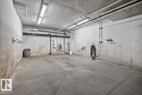 Concrete flooring with a central drainage system, exposed overhead piping, and fluorescent lighting - #116 237 Youville Dr E Nw, Edmonton, AB - Indoor Photo Showing Garage
