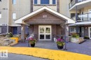 Building entrance featuring a covered portico, glass double doors, outdoor wall lanterns, and a stone-clad facade - #116 237 Youville Dr E Nw, Edmonton, AB  - Outdoor 