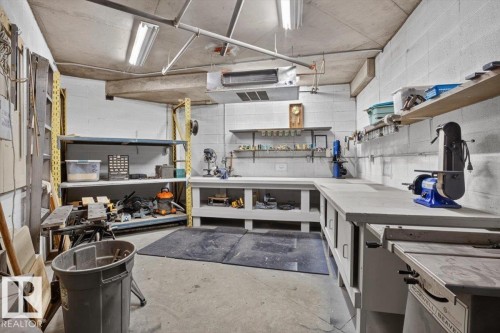 Concrete floor with overhead fluorescent lighting, featuring built-in workbenches, wall-mounted shelving, and a metal storage rack - #116 237 Youville Dr E Nw, Edmonton, AB - Indoor Photo Showing Garage