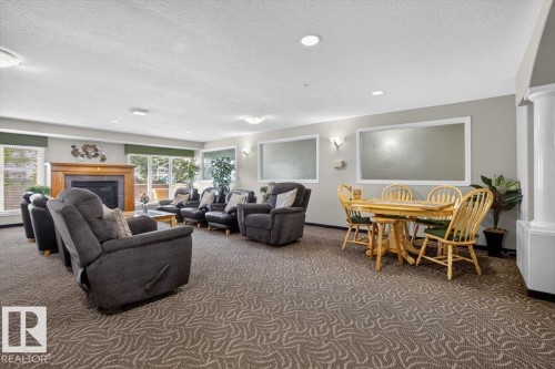 Spacious interior with patterned carpet flooring, a built-in fireplace with a wood-finish mantel, and multiple large windows - #116 237 Youville Dr E Nw, Edmonton, AB - Indoor With Fireplace