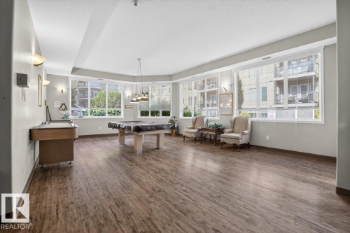 Expansive common area featuring wood-finish flooring, a combination of recessed and wall-mounted lighting, and large windows providing abundant natural illumination - #116 237 Youville Dr E Nw, Edmonton, AB - Indoor