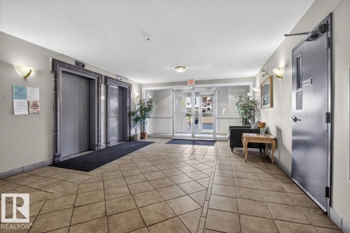 Tiled flooring with a geometric pattern, wall sconces, dual elevators, and a glass-paneled entry door - #116 237 Youville Dr E Nw, Edmonton, AB - Indoor Photo Showing Other Room