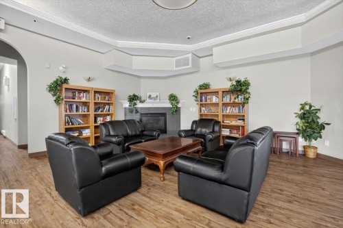 Spacious common area featuring wood-finish flooring, built-in bookshelves, a corner fireplace, and crown molding - #116 237 Youville Dr E Nw, Edmonton, AB - Indoor Photo Showing Other Room