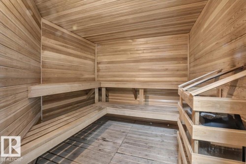 Wood-paneled sauna featuring built-in, tiered bench seating, and a dedicated heating element with a protective wood-slat enclosure - #116 237 Youville Dr E Nw, Edmonton, AB - Indoor Photo Showing Other Room