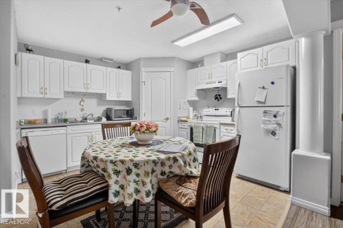 Kitchen featuring white cabinetry, a full suite of white appliances, and tiled flooring - #116 237 Youville Dr E Nw, Edmonton, AB - Indoor