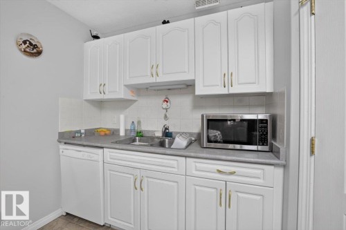 White cabinetry with gold-tone hardware, a stainless steel sink, and light-toned countertops - #116 237 Youville Dr E Nw, Edmonton, AB - Indoor Photo Showing Kitchen With Double Sink