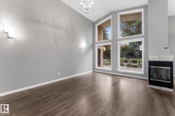 Vaulted ceiling with a contemporary chandelier, expansive windows, wood-finish flooring, and a modern fireplace with a black and stainless steel finish - 