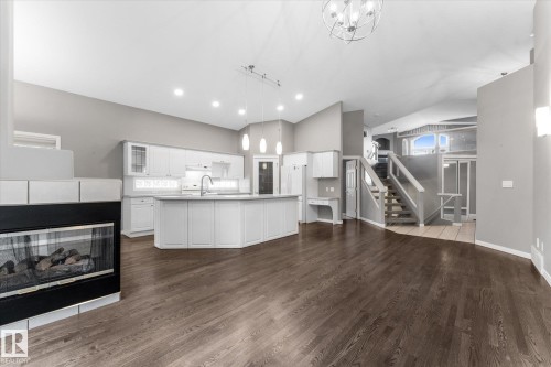 Wood-finish flooring, built-in fireplace, white shaker-style cabinetry, kitchen island with pendant lighting, and a multi-level staircase - 8 Osborne Close, St. Albert, AB - Indoor With Fireplace