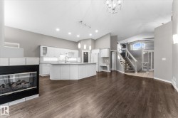 Wood-finish flooring, built-in fireplace, white shaker-style cabinetry, kitchen island with pendant lighting, and a multi-level staircase - 
