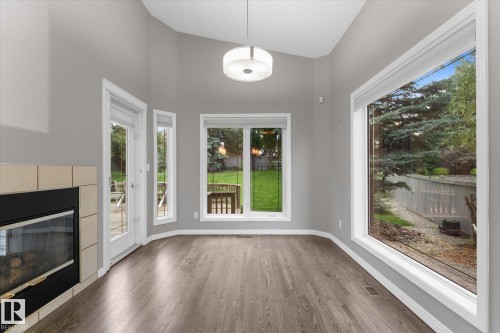 Wood-finish flooring, tiled fireplace surround, expansive windows, vaulted ceilings, and a modern drum pendant light - 8 Osborne Close, St. Albert, AB - Indoor With Fireplace