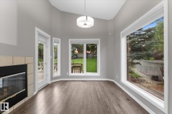 Wood-finish flooring, tiled fireplace surround, expansive windows, vaulted ceilings, and a modern drum pendant light - 