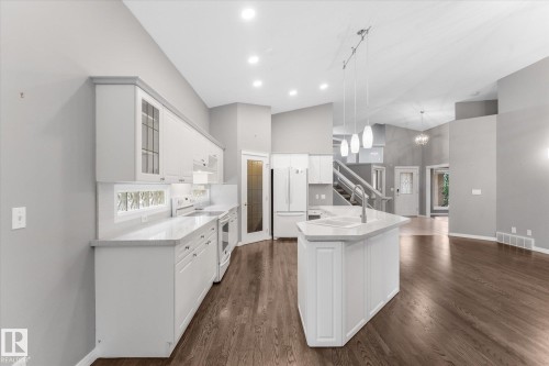 Kitchen featuring white cabinetry, light countertops, integrated sink, pendant lighting, and wood-finish flooring - 8 Osborne Close, St. Albert, AB - Indoor Photo Showing Kitchen
