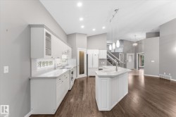 Kitchen featuring white cabinetry, light countertops, integrated sink, pendant lighting, and wood-finish flooring - 