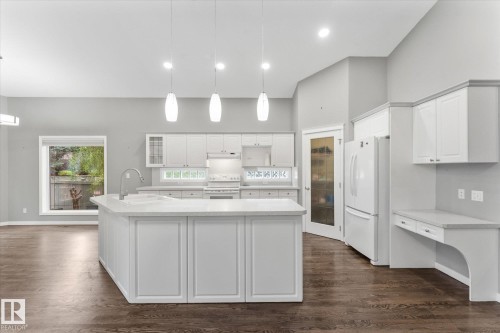 Spacious kitchen featuring an expansive center island with a sink, pendant lighting, built-in cabinetry, and wood-finish flooring - 8 Osborne Close, St. Albert, AB - Indoor Photo Showing Kitchen