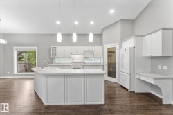 Spacious kitchen featuring an expansive center island with a sink, pendant lighting, built-in cabinetry, and wood-finish flooring - 
