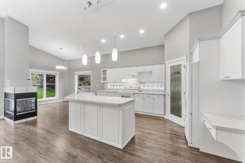 Vaulted ceilings, wood-finish flooring, white cabinetry, a kitchen island with pendant lighting, and a built-in fireplace - 8 Osborne Close, St. Albert, AB - Indoor Photo Showing Kitchen