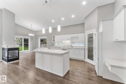 Vaulted ceilings, wood-finish flooring, white cabinetry, a kitchen island with pendant lighting, and a built-in fireplace - 