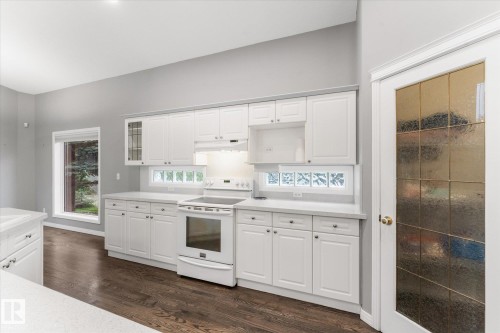 White cabinetry with under-cabinet lighting, wood-finish flooring, recessed ceiling lights, and a paneled glass door - 8 Osborne Close, St. Albert, AB - Indoor Photo Showing Kitchen
