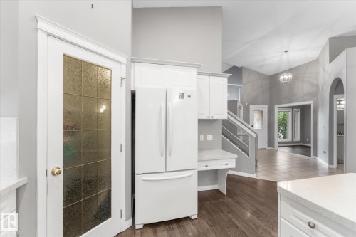 Built-in white cabinetry and refrigerator, wood-finish flooring, and a decorative glass-paneled door - 8 Osborne Close, St. Albert, AB - Indoor Photo Showing Kitchen